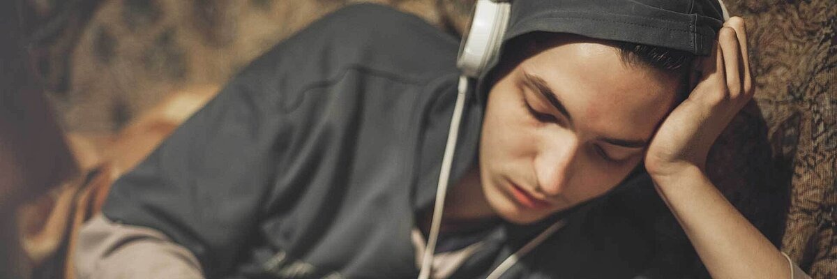 Erschöpfter Teenager in grauem Hoodie lehnt sich an einen Baum