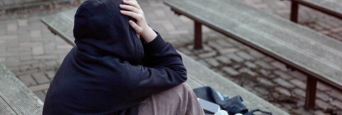 Deprimierter Jugendlicher in schwarzem Hoodie sitzt auf Treppenstufen