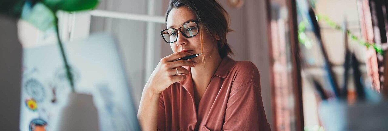 Frau mit Brille sitzt nachdenklich vor einem Laptop
