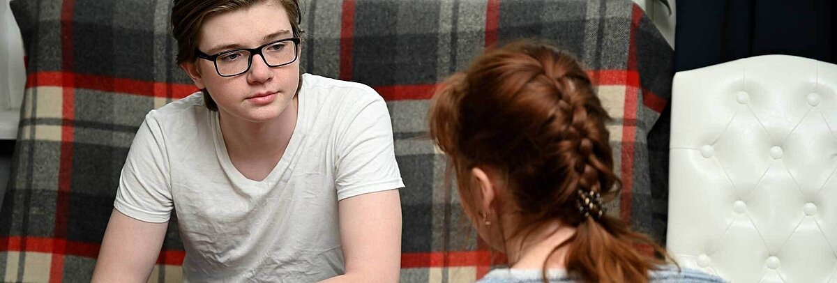Junge mit Brille sitzt auf Couch und hört seiner Mutter zu