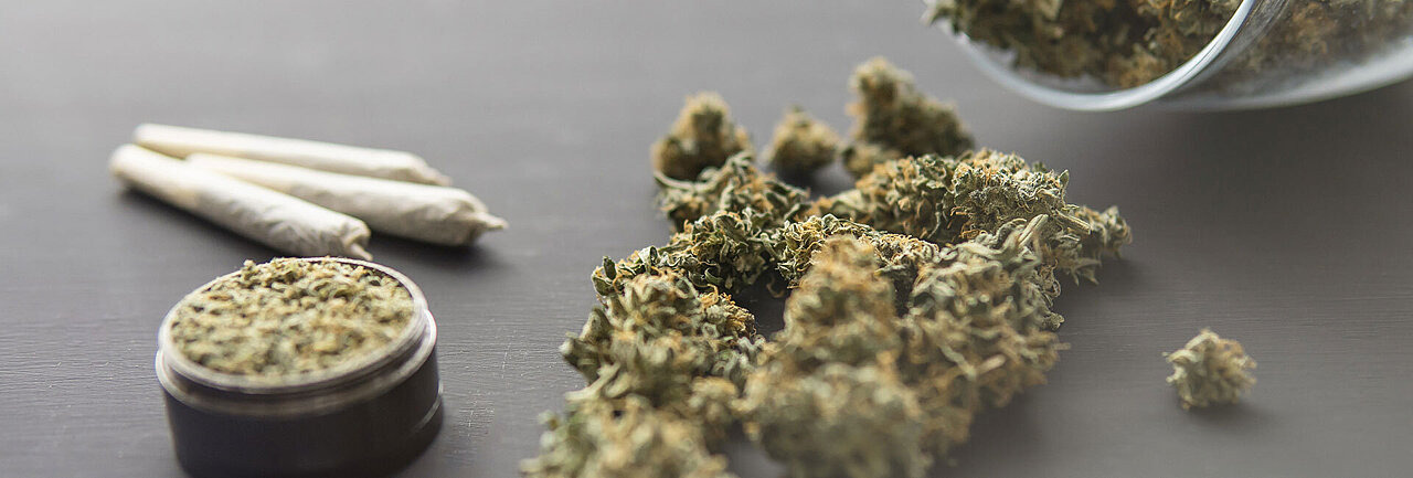 Ansammlung von drei Joints, einer Cannabis-Pouch und mehreren getrockneten Cannabisblüten