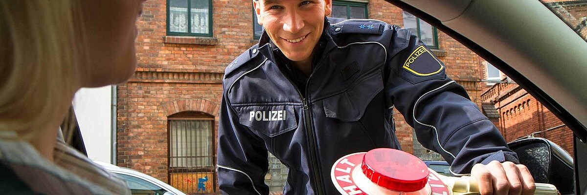 Polizist mit Kelle schaut in ein Autofenster mit einer Frau am Steuer rein