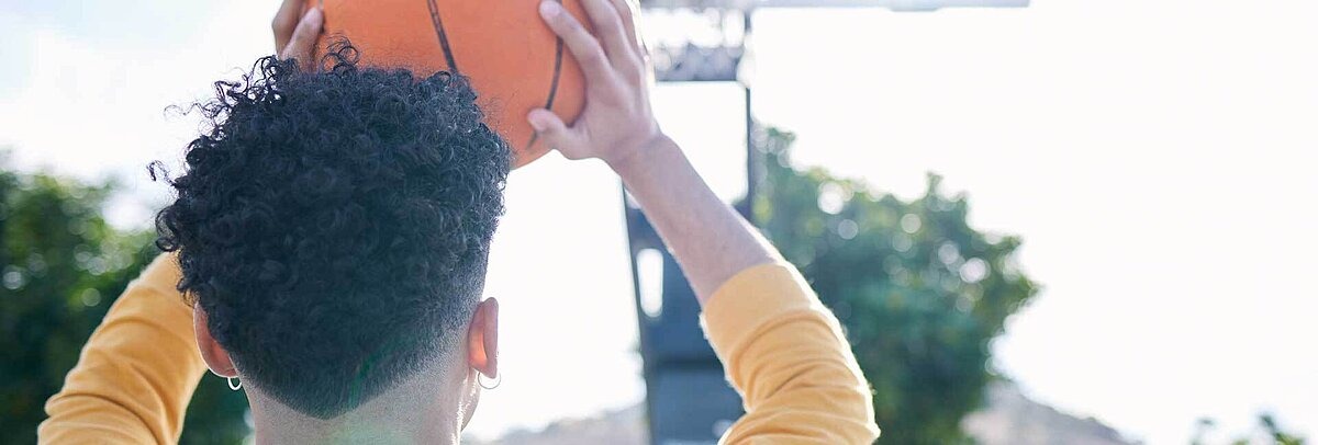 Dunkelhäutiger Teenager zielt mit Basketball auf Korb