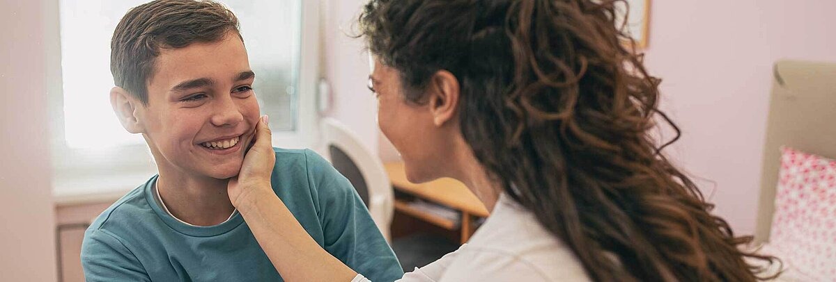 Mutter streichelt ihrem jugendlichen Sohn über die Wange