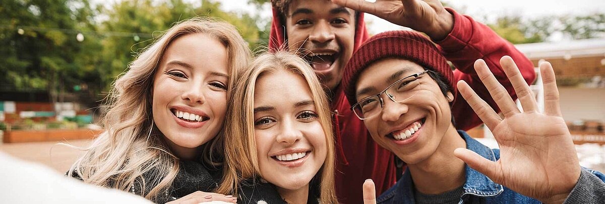 Vier diverse Teenager winken in die Kamera