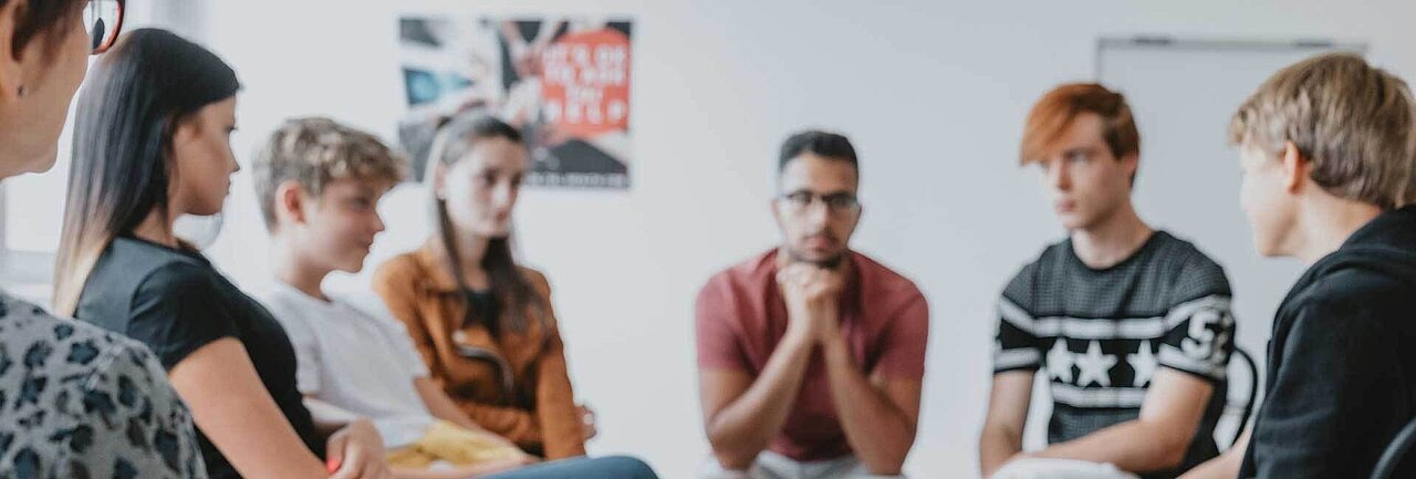 Gruooe Jugendlicher sitzt im Kreis mit einem Lehrer