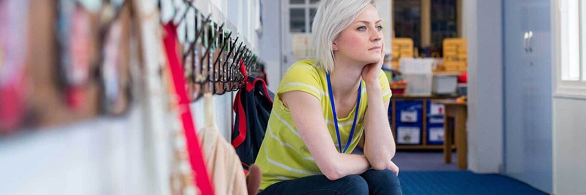 Junge Lehrerin sitzt nachdenklich auf einer Bank im Schulflur