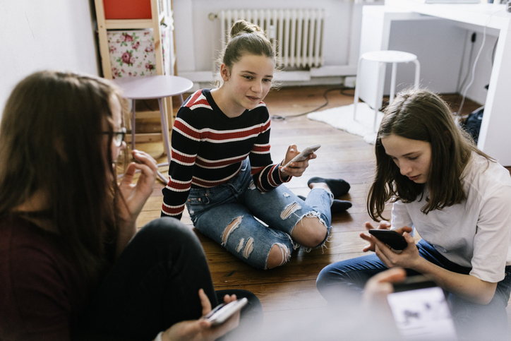 Moodbild "Umgang mit Cannabis" Drei Teenage-Mädchen mit Handys sitzen im Zimmer auf dem Boden