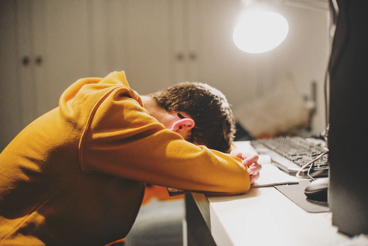 Moodbild "Langfristige Risiken und Sucht" Erschöpfter Teenager im gelben Hoodie liegt mit Kopf auf Tischplatte