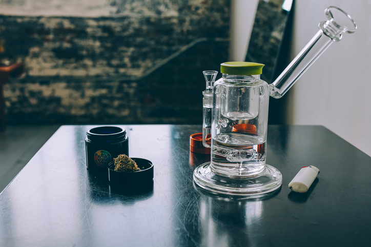 Moodbild "Was bedeutet Kiffen?" Wasserpfeife mit Feuerzeug und getrockneten Cannabisblüten auf einem schwarzen Tisch