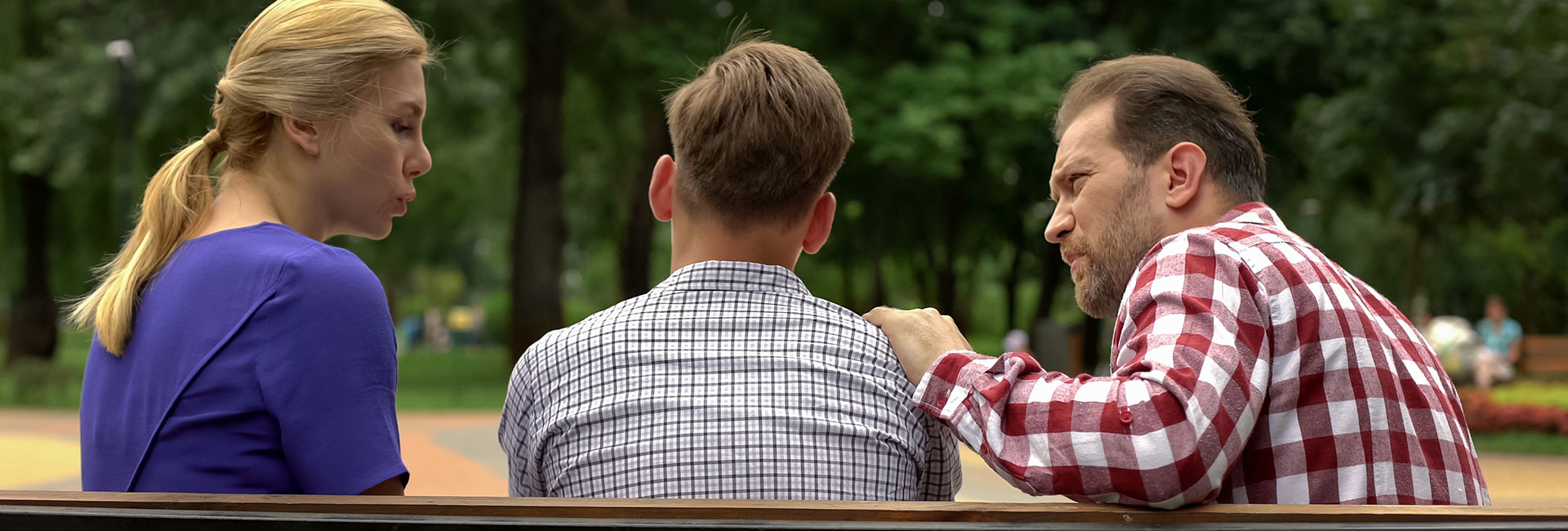 Junge sitzt zwischen Mutter und Vater auf einer Parkbank