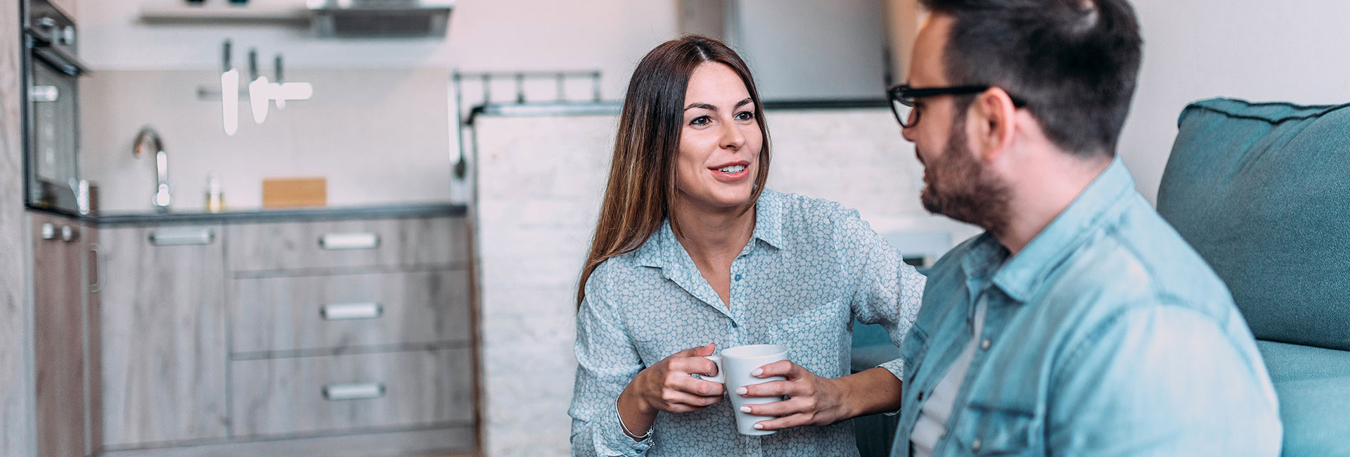 Mann und Frau mit Tasse sitzen auf einer Couch und diskutieren 