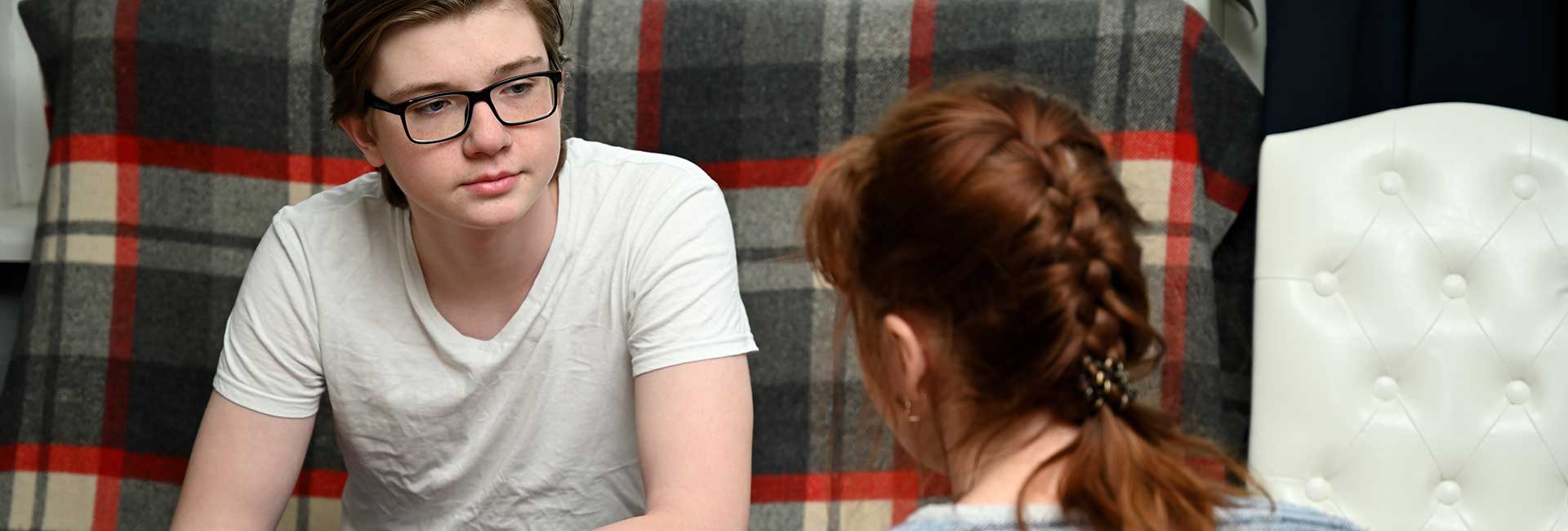 Junge mit Brille sitzt auf Couch und hört seiner Mutter zu