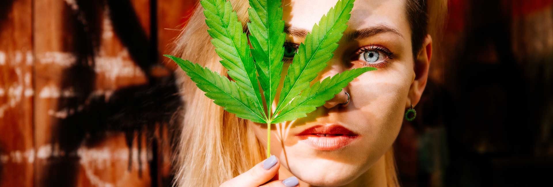 Nahaufnahme eines Mädchens, das sich ein Cannabisblatt vor das Gesicht hält