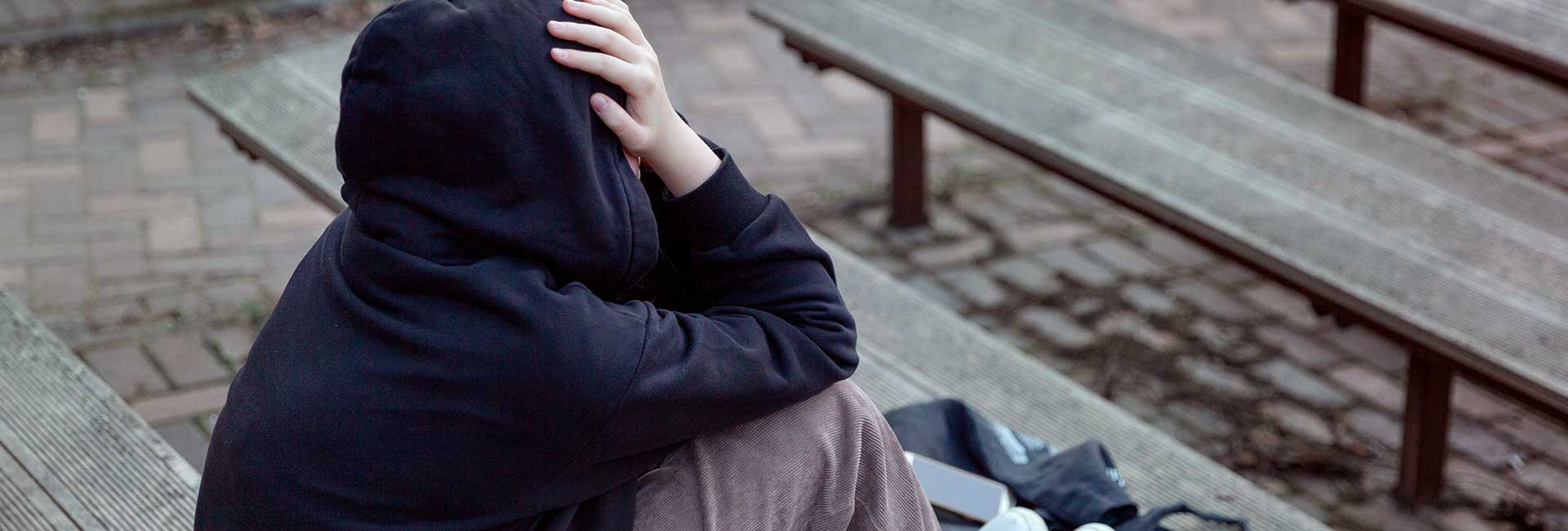 Moodbild "Langfristige Risiken und Sucht" Deprimierter Jugendlicher in schwarzem Hoodie sitzt auf Treppenstufen
