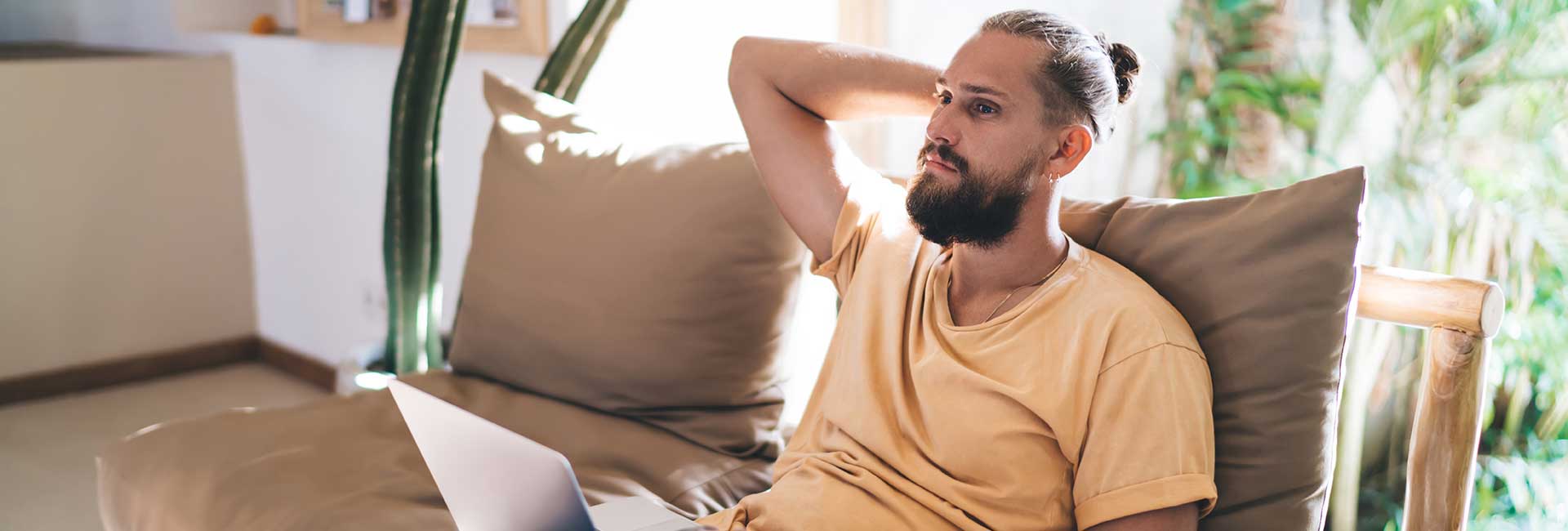 Bärtiger Mann in gelbem T-Shirt sitz nachdenklich auf einer Couch