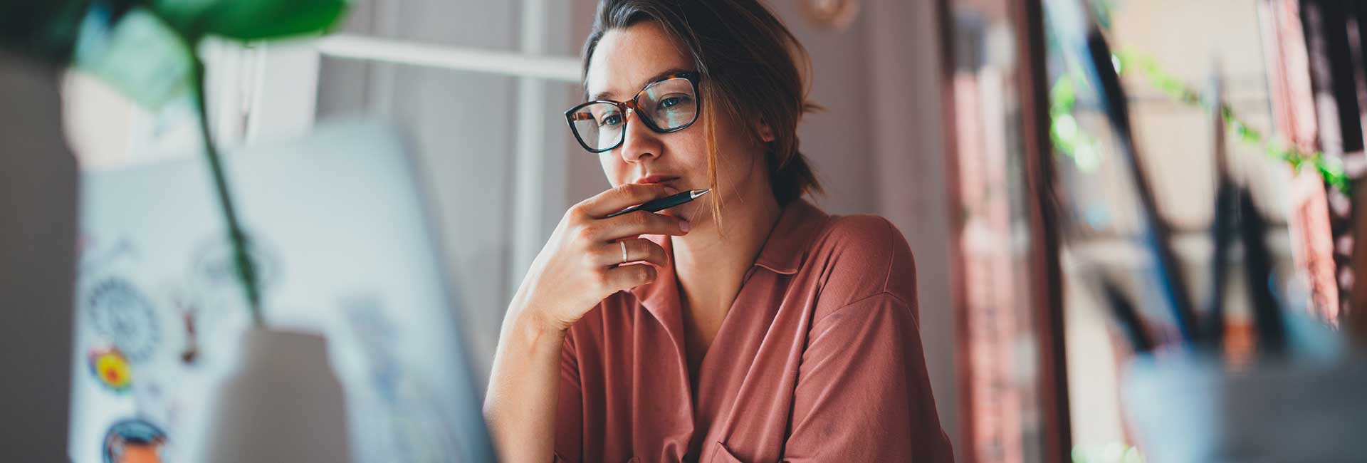 Frau mit Brille sitzt nachdenklich vor einem Laptop